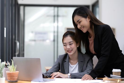 Two young Asian businesswoman discuss investment project working and planning strategy. Business people talking together with laptop computer at office..