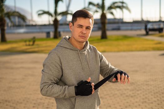 Caucasian man in hoodie bandaging his hands before boxing class outdoors