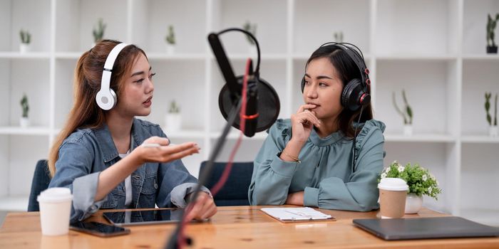 Asian female host recording radio podcast interview with guest at home office.