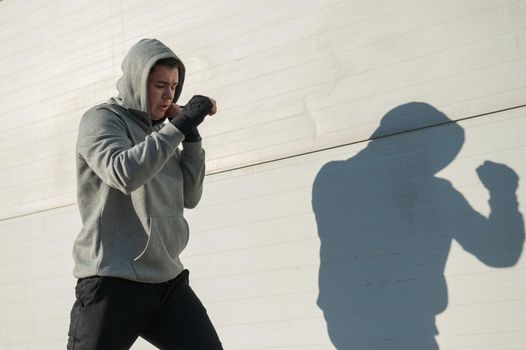 Caucasian man in hoodie is training boxing outdoors