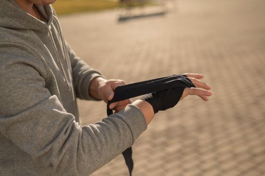 Caucasian man in hoodie bandaging his hands before boxing class outdoors