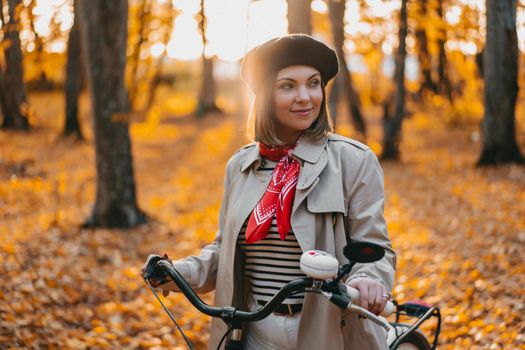 Beautiful dreamy portrait of young smiling woman in french beret cycling alone in park. Sunny day in forest. Trendy lady on vintage bicycle, healthy lifestyle, aesthetic scene. High quality photo