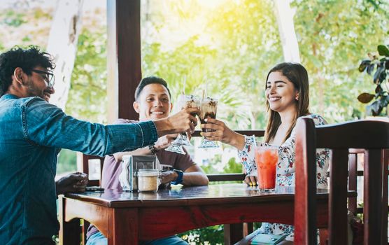 Happy young friends toasting in a coffee shop. Happy friends enjoying a milkshake in a coffee shop. Three happy best friends meeting and toasting in a coffee shop