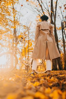 Young woman in classic trench coat rejoices autumn, freedom and beautiful nature. Amazing scene of trendy girl with bicycle. High quality photo