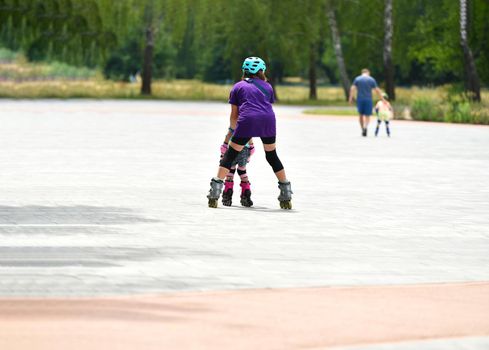 Young mother and her little daughter rollerskating in summer park. happy family have fun. High quality photo