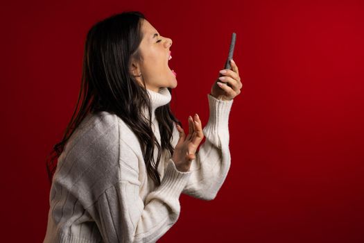 Angry woman screaming down, swears with somebody. Using mobile phone. Stressed and depressed girl on red background.