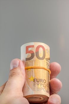 The hand holds a roll of 50 euro banknotes. Euro banknotes rolled up in a white man's hand on a gray background. The concept of financial assistance, real estate purchase, loan or insurance payment