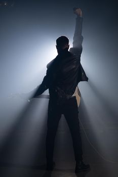 Rock guitarist man on smoky stage and masterfully playing electric guitar. View of musician raises hand up at end as gesture and symbol of success, freedom and victory.