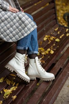 Female legs in a jeans and white fashion boots with laces. fallen leaves on the sidewalk