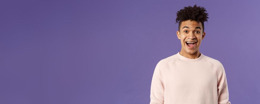 Close-up portrait of enthusiastic, excited and surprised hispanic guy hear amazing news, open mouth beaming smile from amazement and joy, rejoicing glad for friend achievement, purple background.