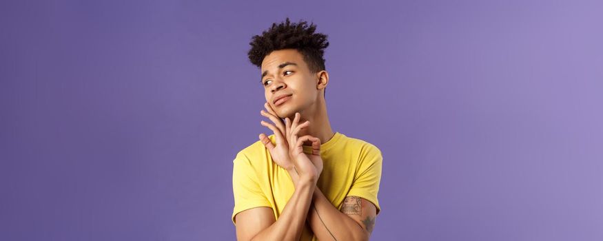 Close-up portrait of glamour beautiful young queer guy with dreads, standing in feminine model pose, gently touching face and looking away sensual, standing purple background.