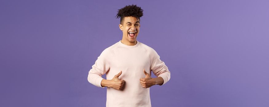 Portrait of enthusiastic lively, attractive young guy winking encourage join team, start career at this company, show thumbs-up with recommendation, give good advice, like and approve.