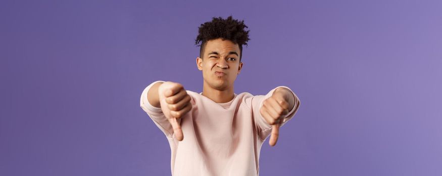 Close-up portrait of disappointed, unimpressed young hispanic man with dreads, grimacing skeptical, judging something bad, watched awful boring movie, show thumbs-down in dislike and disapproval.