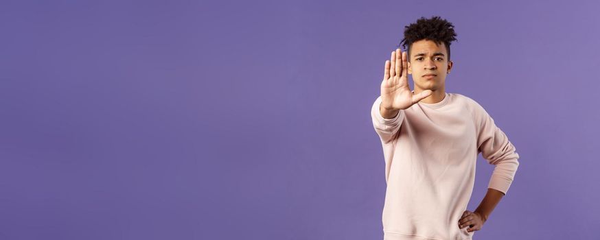 Portrait of confident serious-looking determined young man trying to prevent something, pull hand in stop gesture, look camera assertive, prohibit, give warning or forbid something.