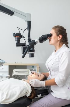 Female dentist using dental microscope treating patient teeth at dental clinic office. Medicine, dentistry and health care concept