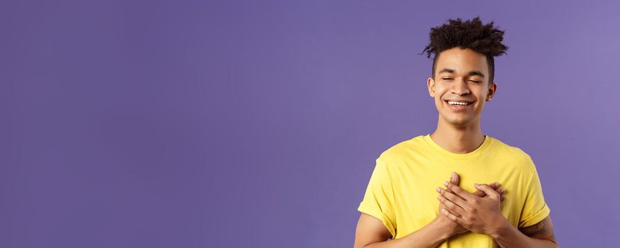 Close-up portrait of happy, upbeat young dreamy guy, remember sweet memories, hold hands on heart, smiling touched and delighted, close eyes grinning, recall romantic moment.