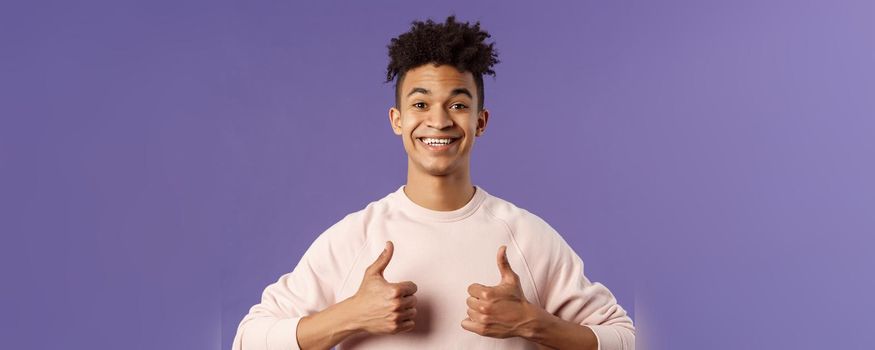 Close-up portrait of enthusiastic handsome young teenage guy, college student recommend awesome courses, online education school, show thumbs-up as recommending, like and approve, smiling.