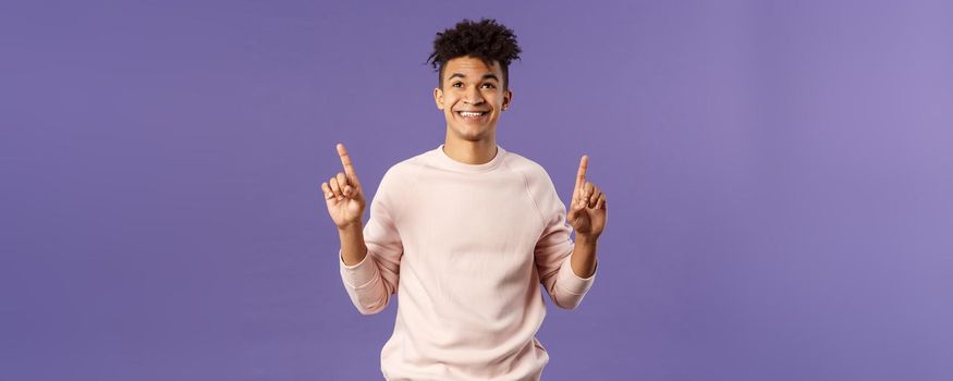 Waist-up portrait of dreamy, handsome 25s young hispanic man seeing good promotion, best deal or offer from online shop, pointing fingers top advertisement, looking up with satisfied smile.