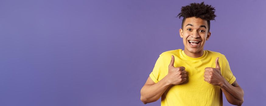 Close-up portrait of enthusiastic healthy hispanic guy staying positive, show thumbs-up and smiling, encourage people stay home, feel fine, like and approve friends plan, standing purple background.