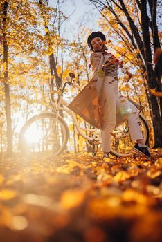 Young pretty woman enjoying autumn nature near vintage white bicycle. Lady having fun on orange nature fall background in park. High quality photo