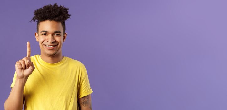 Close-up portrait of funny young teenager, guy picking nose showing index finger and giggle, gagging over his own joke, being nasty and disgusting, standing purple background.