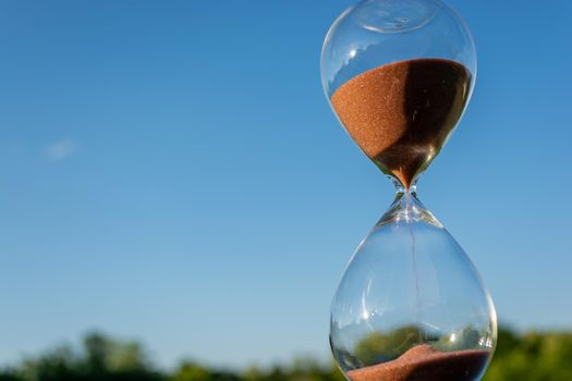 Hourglass against the blue sky on a sunny day. Changeable weather symbol.