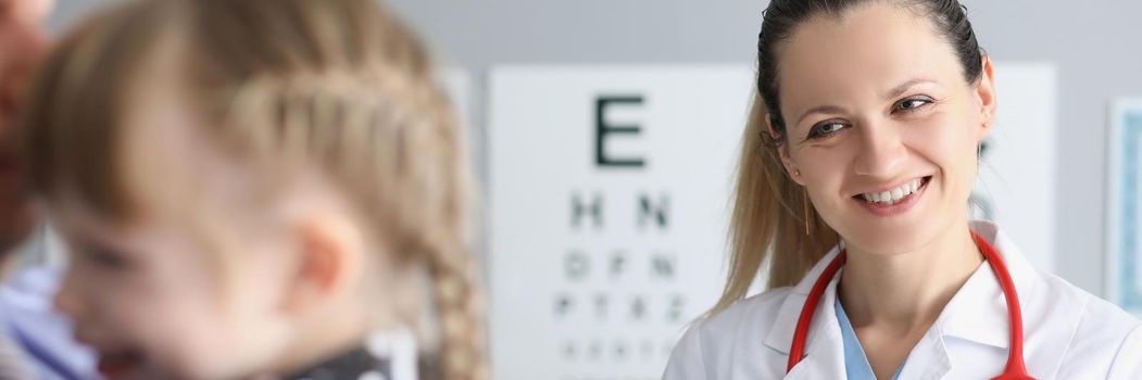 Smiling female doctor standing near little girl in clinic. Medical care for children concept