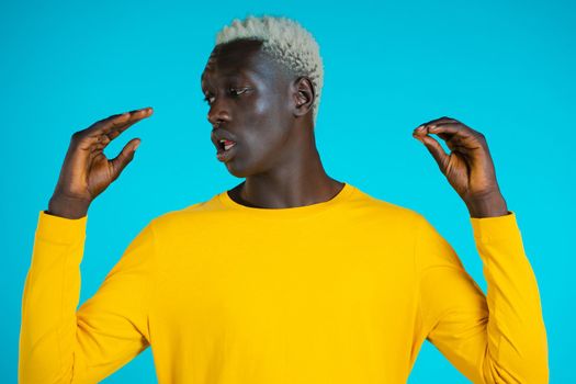 African american bored man showing bla-bla-bla gesture with hands and rolling eyes isolated on blue background. Empty promises, blah concept. Lier.