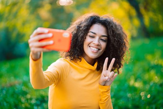 Beautiful african american woman holding and using smart phone to film herself outdoor. Black female using technology networking on holiday, lifestyle