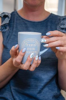 a young woman holds a blue cup of coffee, a beautiful summer manicure. High quality photo