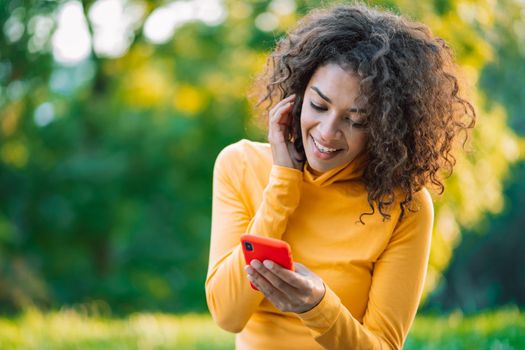 African woman using mobile phone over green background. Girl with curly hairstyle holding smartphone. Black female using technology