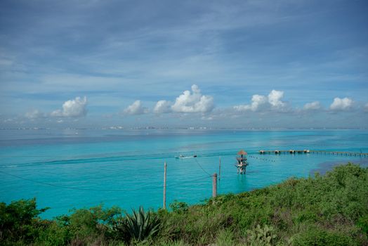 Sandy Caribbean Sea beach with azure water and thatched hut on the horizon.