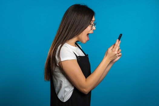 Angry asian woman screaming down, swears with somebody. Using mobile phone. Stressed and depressed girl on blue background.