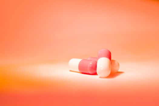 Three red white pill capsules in a slide on an orange background with a gradient. Pharmacy and medicine theme.