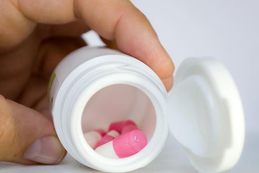 A plastic jar with white-pink pills capsules in a person's hand. Medicine and pharmaceuticals.