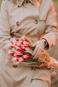 woman in classic trench coat holding bouquet of red tulips. Girl on date. International Women's Day. Congratulations concept. High quality photo