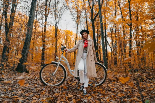 Young woman in classic trench coat with retro bicycle in yellow autumn park. Amazing scene of trendy girl on nature background. Environmentally friendly mode of transport. High quality photo