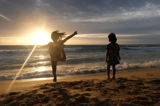 Cute Asian sisters playing on the beach during summer vacation at sunset together. Summer family trip to the beach. travel and vacation concept.