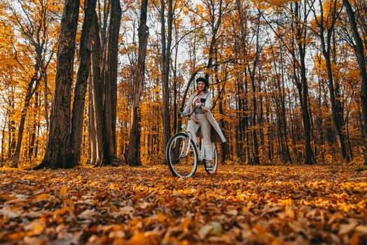Young woman riding on retro bicycle in yellow autumn park. Amazing scene of trendy girl on nature background. Environmentally friendly mode of transport. High quality photo