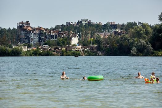 Irpin, Kyiv region, Ukraine - 25 August, 2022: Citi after the Russian occupation. People are having rest near lake opposite destroyed houses