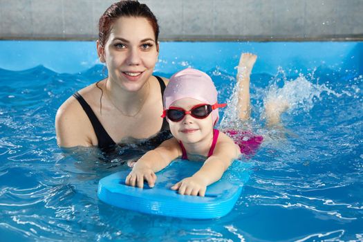 Little girl learning to swim in indoor pool with pool board. Swimming lesson. Active child swims in water