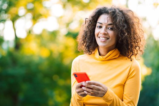 African woman using mobile phone over green background. Girl with curly hairstyle holding smartphone. Black female using technology