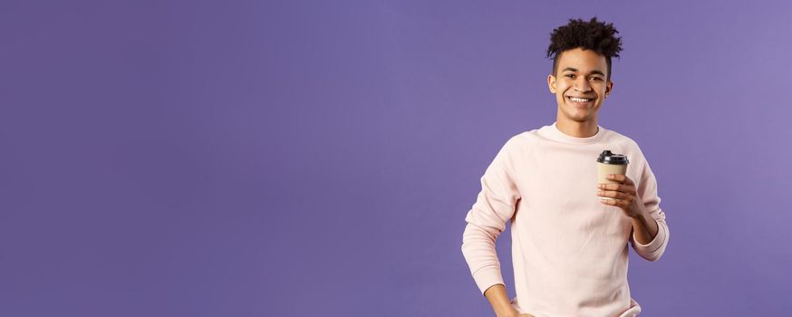 Lifestyle, cafe, eating-out concept. Portrait of cheerful young hispanic guy holding take-away cup of coffee, drinking and smiling camera, waiting for someone, thanking coworker for bringing cappucino.