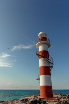 Top of a white-red lighthouse against a blue sky with an airplane. Mexico.