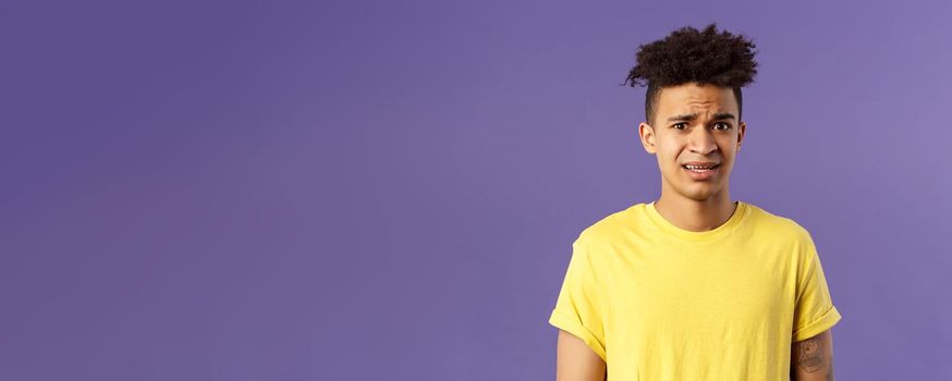 Close-up portrait of awkward and embarrassed young hispanic guy looking nervous, meeting girlfriend parents, stare scared and with panic, feeling concerned, cringe over purple background.