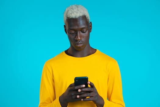 Handsome african man using smartphone on blue studio wall. Using modern technology - apps, social networks