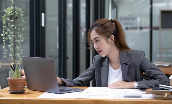 Beautiful young asian woman sitting at coffee shop using laptop. Happy young businesswoman sitting at table in cafe with tab top computer..