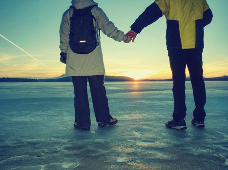 Tourist couple is spending time outdoors on a frozen lake, watching rising sun at horizon.