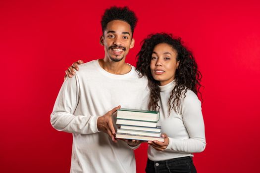 African students on red background in studio holds stack of university books from library. Classmates smiles, they happy to graduate