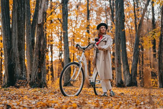 Young woman in classic trench coat with retro bicycle in yellow autumn park. Amazing scene of trendy girl on nature background. Environmentally friendly mode of transport. High quality photo